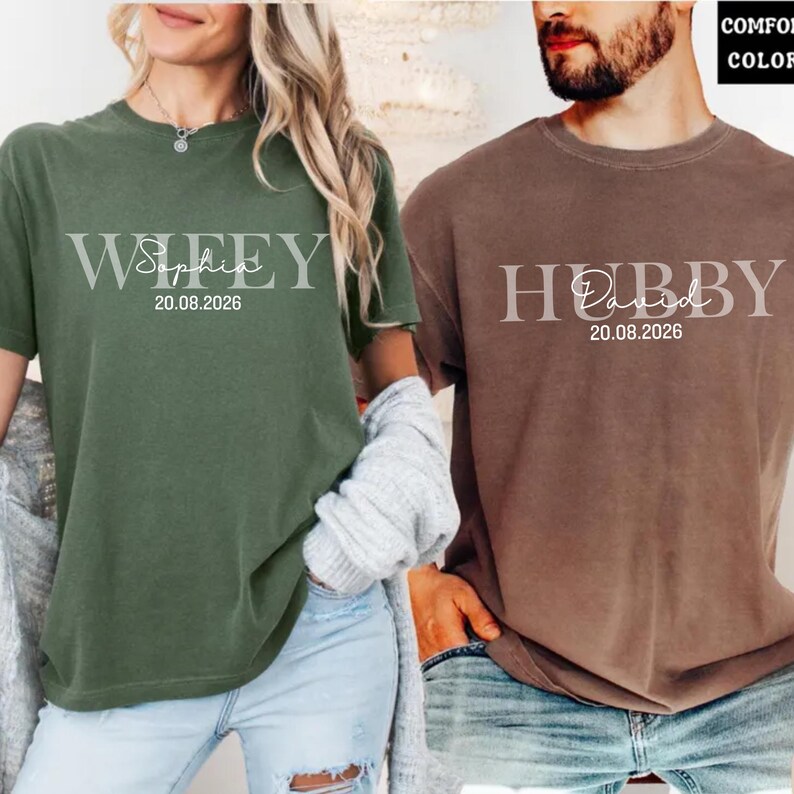 May include: Two short-sleeved t-shirts, one olive green and one brown. The olive green shirt says "Wifey Sophia 20.08.2026" in a light gray font. The brown shirt says "Hubby David 20.08.2026" in a light gray font.