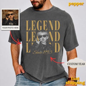 Puede incluir: Una camiseta gris carb&oacute;n de manga corta con un gran estampado gr&aacute;fico de un ni&ntilde;o con gafas de sol y chaqueta de cuero. El texto LEGEND aparece en letras doradas grandes, con el texto Since 1993 escrito debajo de la imagen.