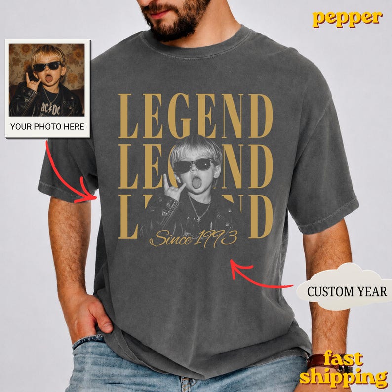 Puede incluir: Una camiseta gris carb&oacute;n de manga corta con un gran estampado gr&aacute;fico de un ni&ntilde;o con gafas de sol y chaqueta de cuero. El texto LEGEND aparece en letras doradas grandes, con el texto Since 1993 escrito debajo de la imagen.