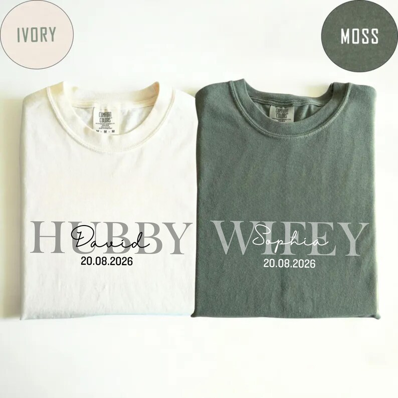 May include: Two Comfort Colors t-shirts, one ivory and one moss green, are displayed. The ivory shirt says "Hubby David 20.08.2026" and the moss green shirt says "Wifey Sophia 20.08.2026". The shirts are folded.