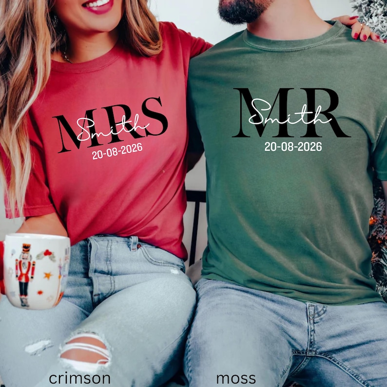 May include: Crimson and moss green t-shirts with matching text. The crimson shirt reads "MRS Smith 20-08-2026" in black script. The moss green shirt reads "MR Smith 20-08-2026" in black script. Both shirts are short-sleeved.
