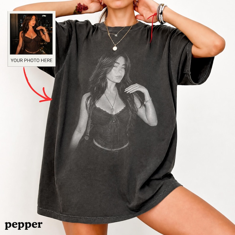Puede incluir: Una camiseta gris carb&oacute;n de corte oversize con una gran impresi&oacute;n fotogr&aacute;fica en blanco y negro de una persona con un top tipo cors&eacute; y un collar. Un peque&ntilde;o recuadro en la esquina superior izquierda muestra la misma foto con el texto YOUR PHOTO HERE.