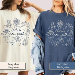 May include: Two t-shirts, one ivory and one navy blue, featuring a white graphic. The design includes champagne flutes, flowers, doves, a ring, and the text "future mrs. smith". The ivory shirt has a navy print, and the navy shirt has a white print.