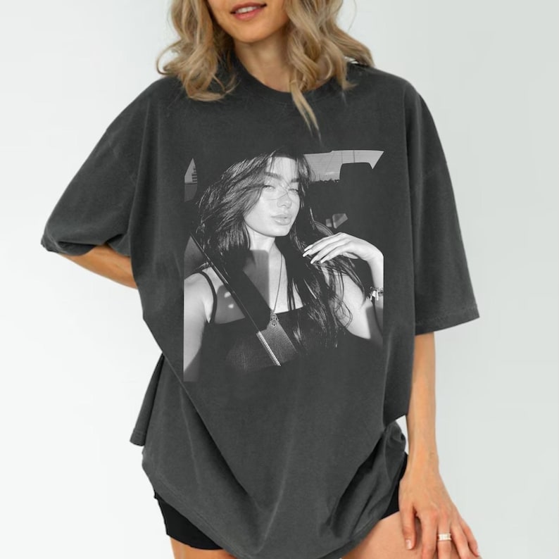 May include: Dark gray oversized t-shirt featuring a black and white image of a woman. The image on the shirt shows a woman with long hair, wearing a black top. The shirt has short sleeves and a relaxed fit.