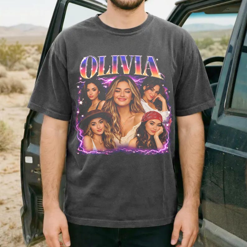 May include: Dark grey t-shirt with the name "OLIVIA" in a retro font with a colourful gradient effect. The shirt features a graphic of several women in various poses, framed by a purple outline.