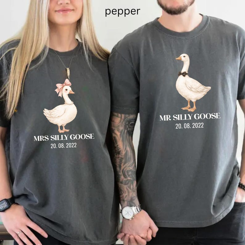 Peut inclure: Deux t-shirts gris fonc&eacute; assortis. L'un pr&eacute;sente une oie avec un n&oelig;ud rose et le texte "MRS SILLY GOOSE 20.08.2022". L'autre a une oie avec un n&oelig;ud noir et le texte "MR SILLY GOOSE 20.08.2022".