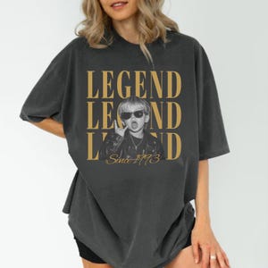 Puede incluir: Una camiseta gris carb&oacute;n de corte oversize con un estampado gr&aacute;fico de un ni&ntilde;o con gafas de sol y chaqueta de cuero. El texto "LEGEND" aparece en grandes letras doradas sobre y bajo la imagen, con el texto "Since 1993" en cursiva debajo.