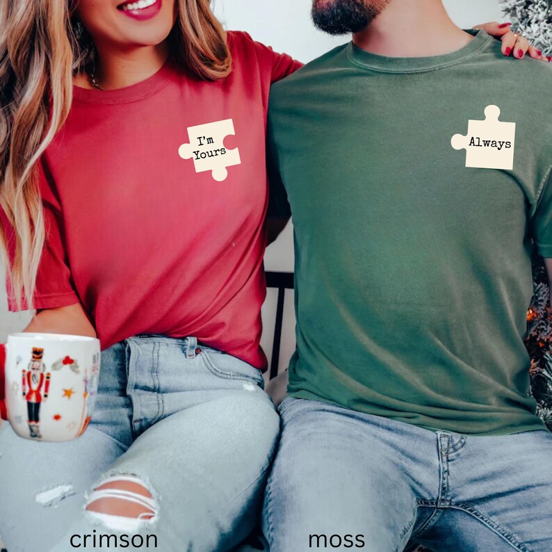 May include: Crimson and moss green matching t-shirts. The crimson shirt has a puzzle piece with "I'm Yours" printed on it. The moss green shirt has a puzzle piece with "Always" printed on it. Both shirts are short-sleeved.