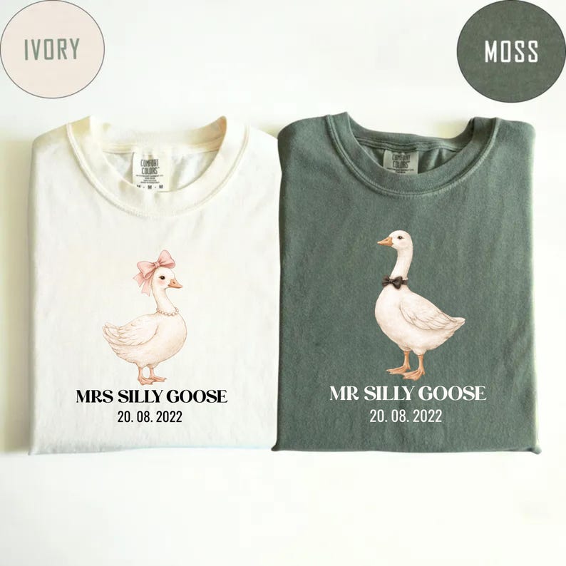 Peut inclure: Deux t-shirts, un ivoire et un vert mousse, chacun avec une illustration d'oie. Le t-shirt ivoire pr&eacute;sente une oie avec un n&oelig;ud rose et le texte "MRS SILLY GOOSE 20.08.2022". Le t-shirt vert affiche une oie avec un n&oelig;ud noir et le texte "MR SILLY GOOSE 20.08.2022".