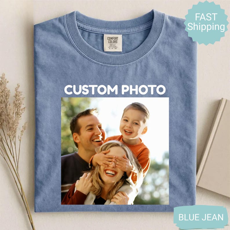 May include: Blue jean colored t-shirt with a custom photo design. The photo features a family of three, with the text "CUSTOM PHOTO" above the image. The shirt has a crew neck and a Comfort Colors tag.
