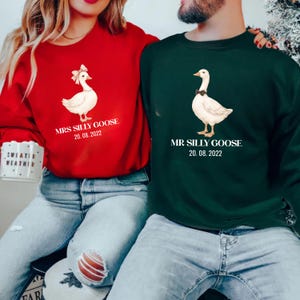 Peut inclure: Sweat-shirts rouges et verts avec des motifs d'oies. Le sweat-shirt rouge pr&eacute;sente une oie avec un n&oelig;ud et le texte "MRS SILLY GOOSE 20.08.2022". Le sweat-shirt vert montre une oie avec un n&oelig;ud papillon et le texte "MR SILLY GOOSE 20.08.2022".