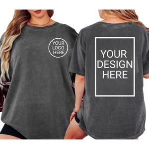 Puede incluir: Dos camisetas gris carb&oacute;n. Una camiseta tiene un logotipo circular que dice "YOUR LOGO HERE". La otra camiseta tiene un dise&ntilde;o rectangular que dice "YOUR DESIGN HERE".