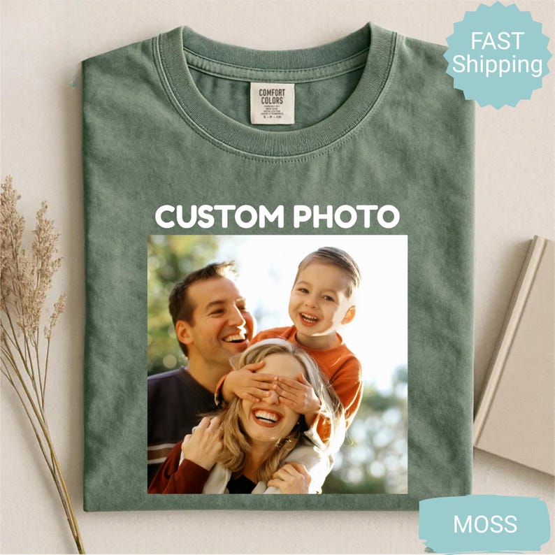 May include: Moss green t-shirt with a custom photo design. The photo features a family of three, with the text "CUSTOM PHOTO" in white. The shirt has a crew neck and short sleeves. The shirt is made of a soft, comfortable material.