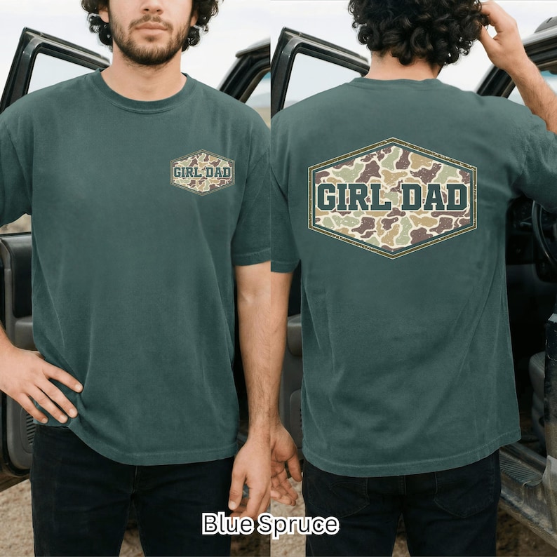 May include: Blue Spruce short-sleeved t-shirt with "GIRL DAD" text in a camouflage design on the front and back. The shirt has a crew neck and a relaxed fit. The text is in a vintage style.