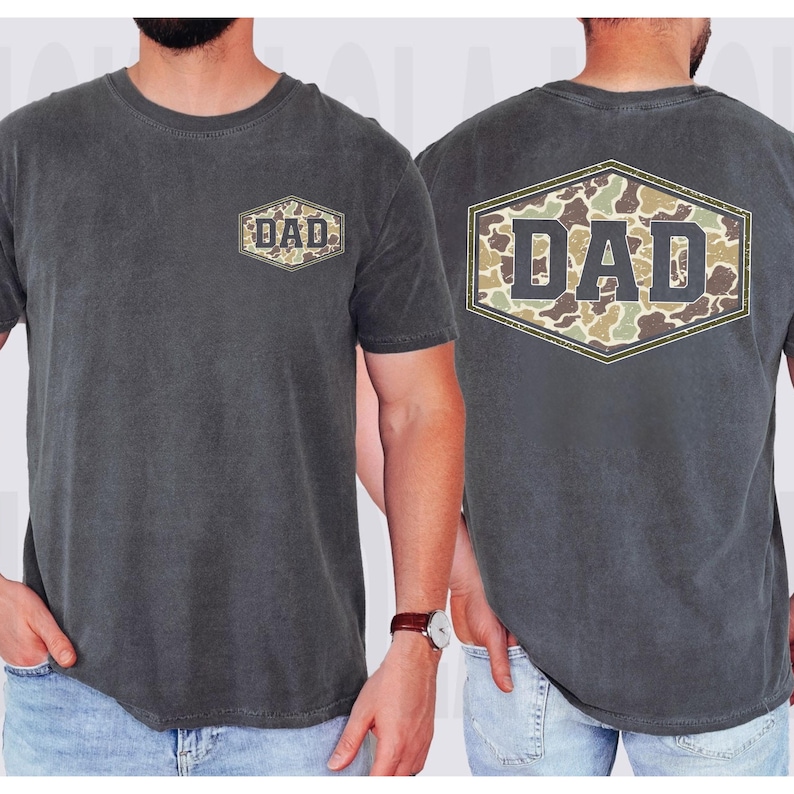 May include: Charcoal gray t-shirt with the word "DAD" in a camouflage design on the front and back. The shirt has a crew neck and short sleeves. The "DAD" design is inside a hexagon shape.