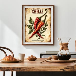 K&ouml;nnte beinhalten: Ein gerahmter Druck mit zwei roten Chilischoten mit gr&uuml;nen Stielen und Bl&auml;ttern, vor einem Hintergrund im Vintage-Stil. Das Wort "CHILLI" steht oben, mit dem Satz "FOR THE BOLD AND BRAVE IN THE KITCHEN" unten.