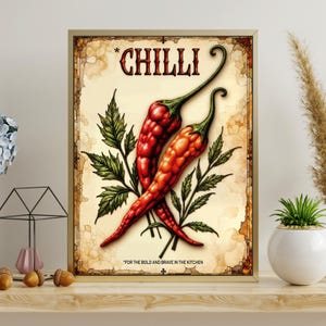 K&ouml;nnte beinhalten: Ein gerahmter Druck mit zwei roten Chilischoten mit gr&uuml;nen Stielen und Bl&auml;ttern, vor einem Hintergrund im Vintage-Stil. Das Wort "CHILLI" steht oben, mit dem Text "FOR THE BOLD AND BRAVE IN THE KITCHEN" unten.