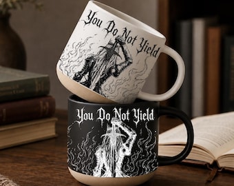 May include: Two ceramic mugs with a tan base and a handle. The top mug is white with black ink illustrations of a figure holding a sword amidst flames and the text "You Do Not Yield." The bottom mug is black with white ink of the same design.