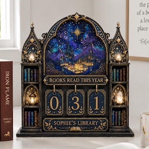 May include: A decorative black and gold bookshelf tracker with a starry night mountain scene, featuring the text "BOOKS READ THIS YEAR" and "SOPHIE'S LIBRARY" with three hanging number tiles currently displaying 0, 3, and 1.