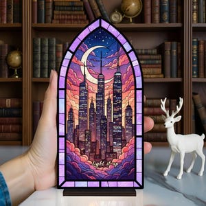 May include: A stained glass panel depicting a cityscape at night, with a crescent moon and stars. The panel is framed in purple and has the words "Light it up" at the bottom. The panel is set on a wooden base.