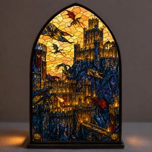 May include: Stained glass lamp depicting a fantasy castle scene with dragons. The artwork shows a fortress with towers, flags, and dragons in a sunset sky. The lamp has a black base and a gothic arch shape.