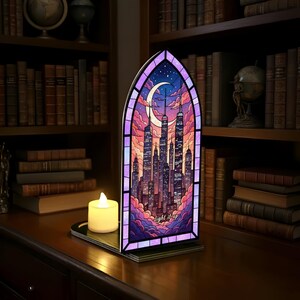 May include: A stained-glass style panel depicting a cityscape with a crescent moon and clouds, framed in purple. The panel is lit from behind, with the text "light it up" at the bottom. A battery-operated candle sits in front of the panel.
