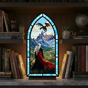 May include: A stained glass panel depicting a fantasy scene with a figure in black and red, facing a dragon in flight over mountains and a valley. The panel has a blue border and is set in a wooden frame.