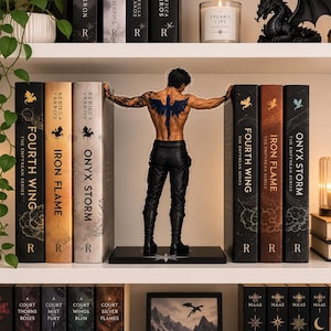 May include: An acrylic bookend featuring a shirtless male figure with a large blue dragon tattoo on his back, wearing black pants and boots, positioned between two sets of books titled Fourth Wing, Iron Flame, and Onyx Storm.