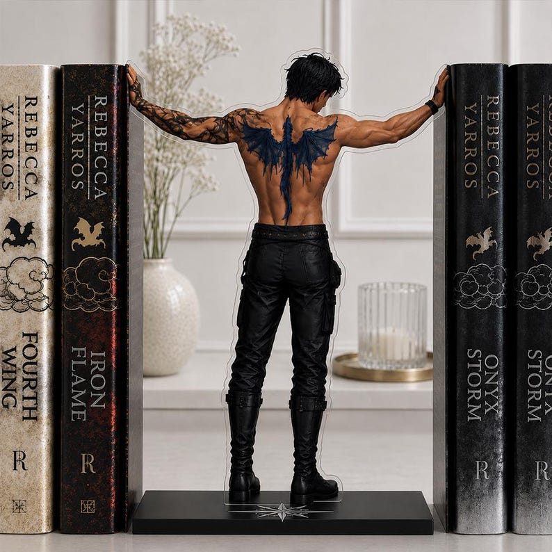 May include: An acrylic standee featuring a shirtless male figure with a dark dragon tattoo on the back, wearing black pants and boots, positioned between two pairs of bookends labeled Fourth Wing, Iron Flame, and Onyx Storm by Rebecca Yarros.