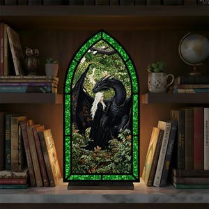 May include: A stained glass-style lamp featuring a black dragon and a figure with long white hair, set against a green and forest background. The lamp has a green border and sits on a wooden base, with a warm glow illuminating the scene.