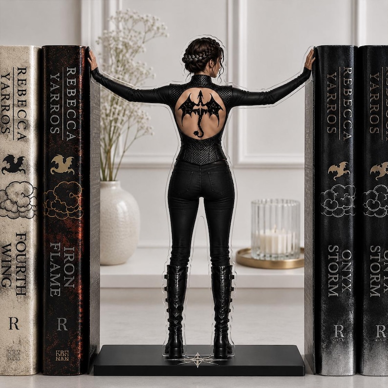 May include: A clear acrylic standee featuring a figure in a black long-sleeved top with a circular back cutout displaying a dragon tattoo, black pants, and black boots, positioned between two large book-shaped decorative bookends.
