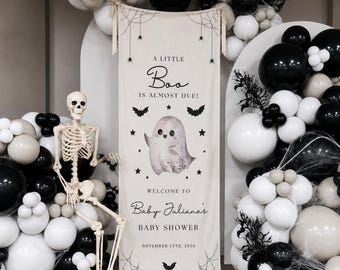 May include: A vertical cream-colored fabric banner featuring a central illustration of a ghost, black bats, stars, and spiderwebs. The text reads A LITTLE Boo IS ALMOST DUE! WELCOME TO Baby Juliana's BABY SHOWER NOVEMBER 15TH, 2026.