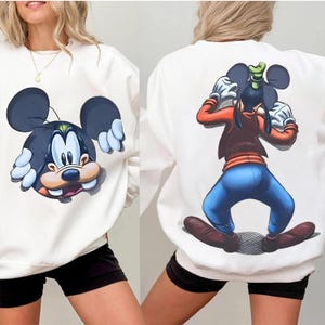 May include: White sweatshirt featuring a cartoon illustration of Mickey Mouse on the front and Goofy on the back. The Mickey Mouse graphic has a black and blue color scheme. The Goofy graphic is in full color with blue pants and a brown jacket.