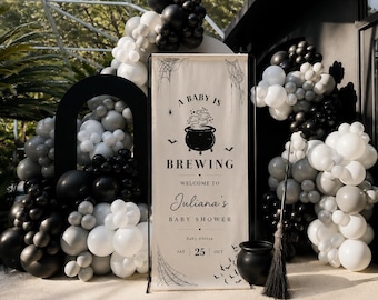 May include: A vertical banner with the text A BABY IS BREWING WELCOME TO Juliana's BABY SHOWER BABY OLOVIA SAT 25 OCT, featuring a black cauldron, spiderwebs, and bats. The banner is surrounded by a large arch of black, white, and gray balloons.