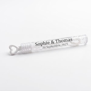 Peut inclure: Un flacon de bulles transparent avec une poignée en forme de cœur. Le flacon porte l'inscription "Sophie & Thomas 20 Septembre 2025". Le flacon est sur fond blanc.