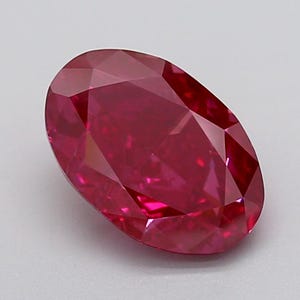 May include: A faceted, oval-cut ruby gemstone. The gem is a deep, saturated red color with multiple reflective facets. The gemstone is set against a neutral background.