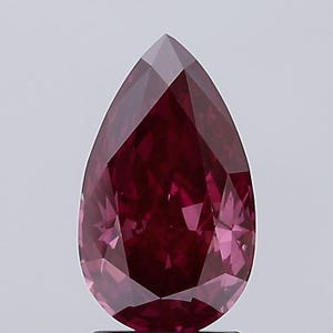 May include: A faceted, pear-shaped gemstone with a deep red hue. The gem's surface reflects light, showcasing its multiple facets and internal structure. The overall shape is elongated, with a pointed tip and a rounded base.