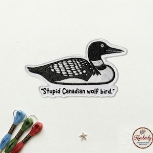 May include: Embroidered patch featuring a black and white loon with the text "Stupid Canadian wolf bird." The patch has a white border and is on a white background. The patch is a humorous take on the loon.