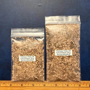 May include: Two clear plastic resealable bags filled with tan-colored 1/8 inch Feldspar resin flakes. The smaller bag is labeled 25 gr and the larger bag is labeled 50 gr, both featuring the text NorthernWestStuff, positioned above a wooden ruler.