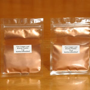 May include: Two clear plastic pouches filled with fine copper leaf bronze powder. Each pouch has a white label with black text indicating the product name, weight (5 gr and 15 gr), and the seller's name.