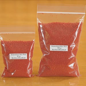 May include: Two clear plastic bags filled with red granulated wax. One bag is labeled "Granulated Wax Red 50 gr NorthernWestStuff", and the other is labeled "Granulated Wax Red 150 gr NorthernWestStuff".