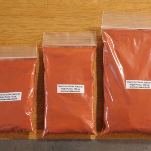 May include: Three clear plastic bags filled with red powder, labeled with white stickers. The bags contain 30g, 100g, and 200g of Red Iron Oxide, Natural, High Purity powder from NorthernWestStuff.