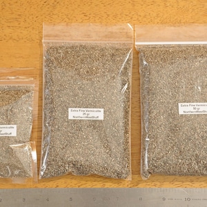 May include: Three clear plastic bags filled with Extra Fine Vermiculite, labeled with weights of 10g, 25g, and 50g. A metal ruler is placed below the bags on a wooden surface.