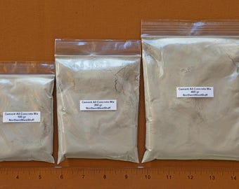 Może przedstawiać: Trzy przezroczyste plastikowe torby z mieszanką cementową, oznaczone jako "Cement All Concrete Mix" o wadze 100g, 200g i 400g. Torby są zamknięte i ułożone na brązowej powierzchni.