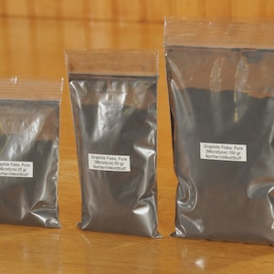 May include: Three clear plastic bags filled with dark gray graphite flakes. The bags are labeled with the product name, weight in grams, and the seller's name. The bags are arranged from smallest to largest, with the smallest containing 25 grams.
