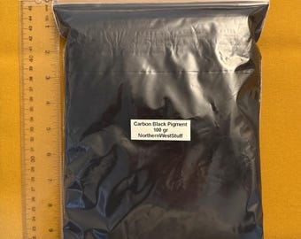 May include: A clear plastic resealable bag filled with fine carbon black pigment powder. A white label on the front reads Carbon Black Pigment 100 gr NorthernWestStuff. A clear plastic ruler is placed along the side and bottom for scale.