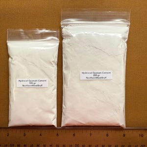 May include: Two clear plastic bags filled with white Hydrocal Gypsum Cement. The smaller bag has a label that reads "100 gr NorthernWestStuff". The larger bag has a label that reads "200 gr NorthernWestStuff". A ruler is at the bottom.
