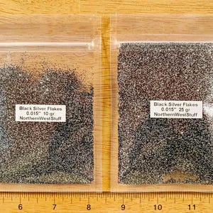 May include: Two clear plastic bags filled with black and silver glitter flakes. The bags have labels that read "Black Silver Flakes 0.015" 10 gr NorthernWestStuff" and "Black Silver Flakes 0.015" 25 gr NorthernWestStuff".