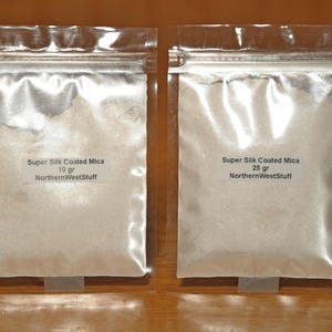 May include: Two clear plastic bags containing Super Silk Coated Mica powder. One bag is labeled 10 gr, the other 25 gr. Both bags have the text "NorthernWestStuff". The bags are sealed and sit on a wooden surface.