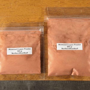 May include: Two clear plastic bags filled with atomized copper powder. The smaller bag contains 100 grams, and the larger bag contains 200 grams. Each bag has a white label with the text "Atomized Copper Powder" and "NorthernWestStuff".